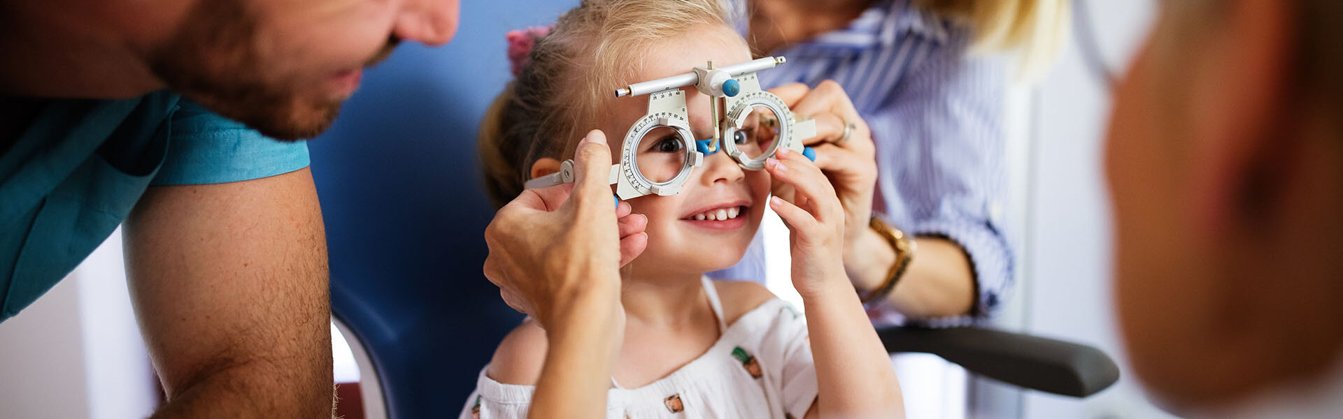 Ophthalmologist is checking the eye vision of little cute girl in modern clinic. Family with daughter in ophthalmology clinic.